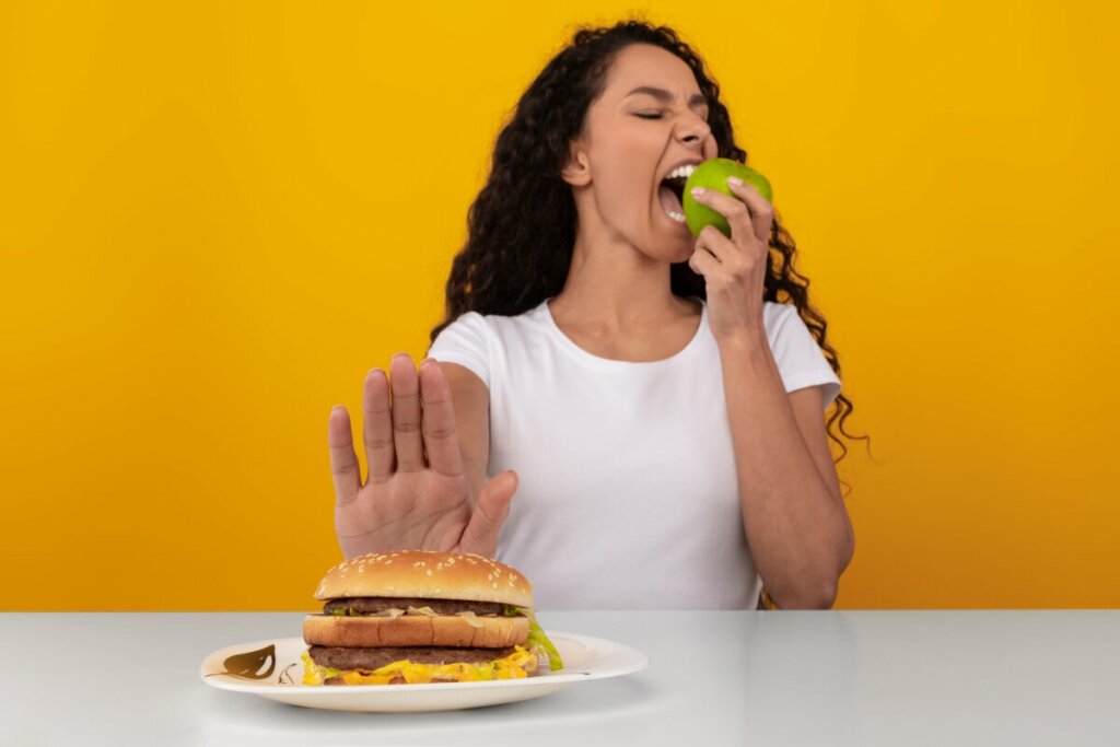 Mulher rejeitando um hambúrguer e comendo uma maçã
