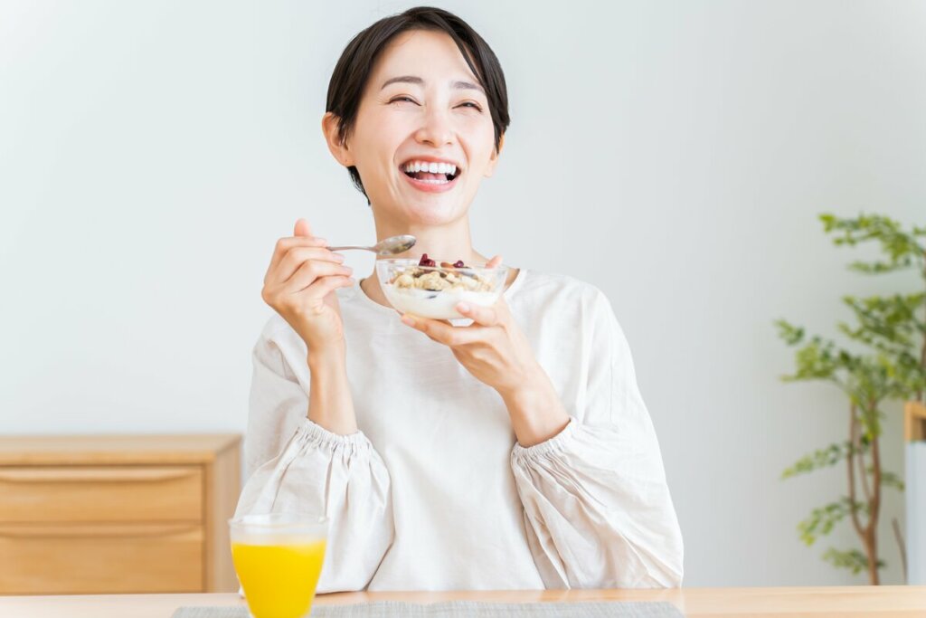 Mulher sentada sorrindo segurando um recipiente com iogurte e cereais 