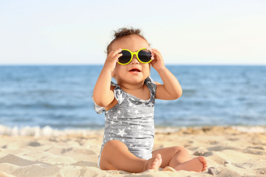 Bebê de óculos escuro sentado na areia da praia