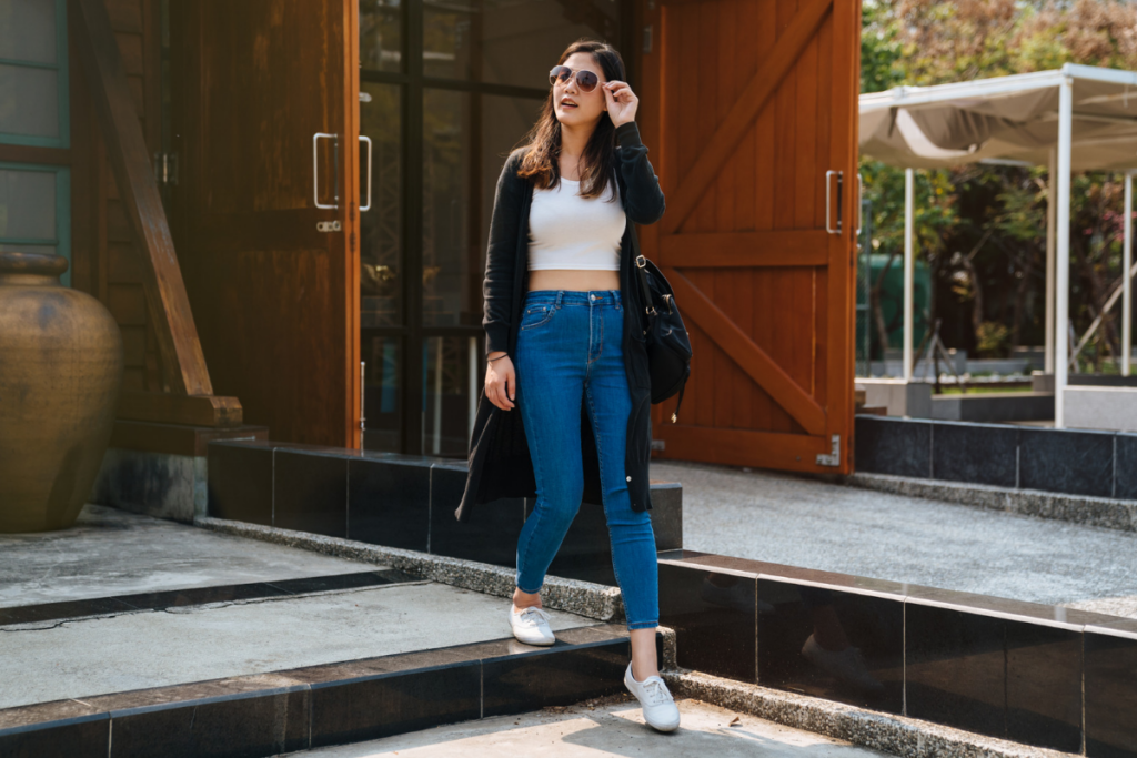 Mulher usando blusa branca, calça jeans e óculos de sol andando na rua