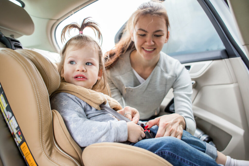 Meninas sentada em uma cadeirinha no carro com uma mulher arrumando o cinto de segurança 