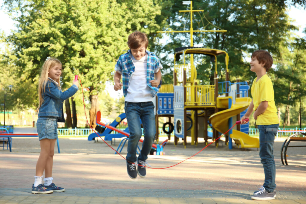 Três crianças em parque brincando de pular corda