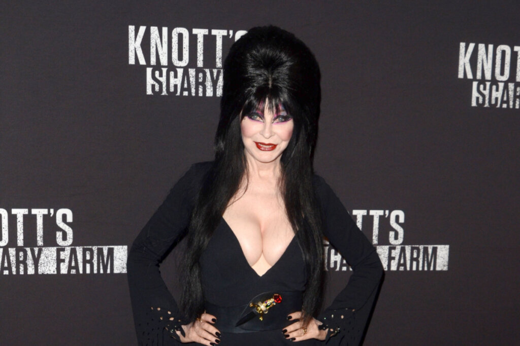 Personagem Elvira com o cabelo preto preso e roupa preta em fundo preto