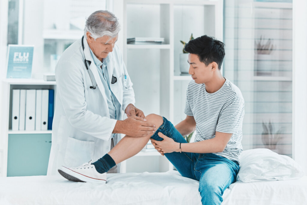 Médico examinando joelho de jovem sentado em maca