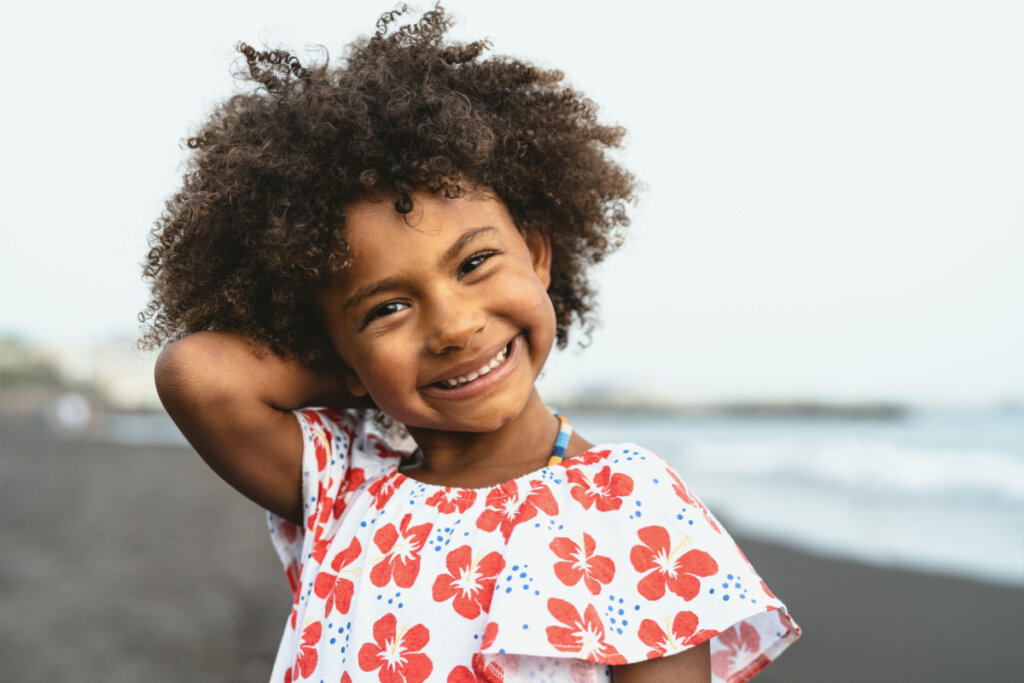 Menina sorrindo de cabelo cacheado solto e com a mão atrás da cabeça