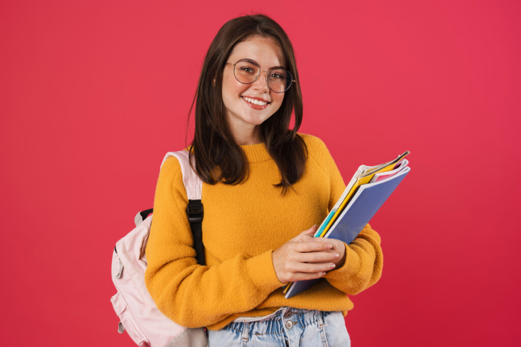Menina sorrindo com mochila nas costas segurando livros