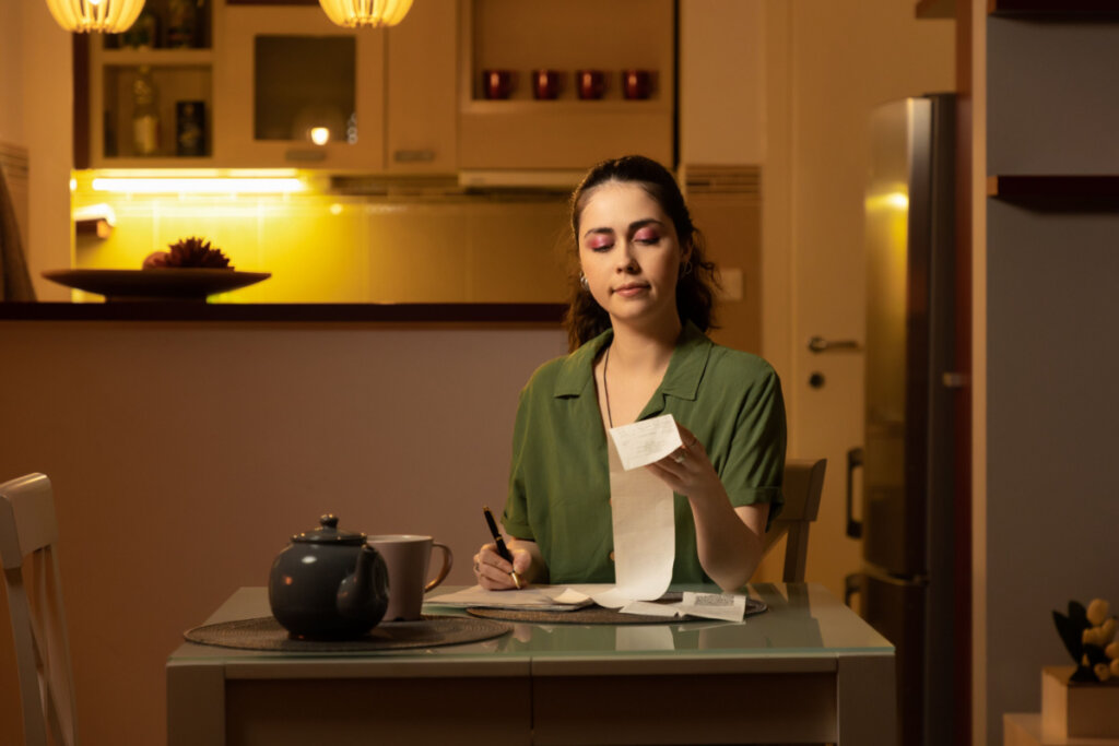 Mulher sentada em mesa da cozinha, anotando gastos 