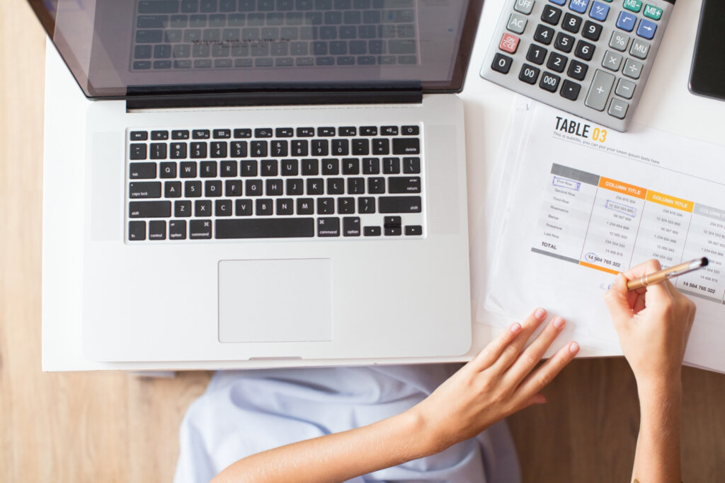 Mulher fazendo contas com notebook, papel e calculadora