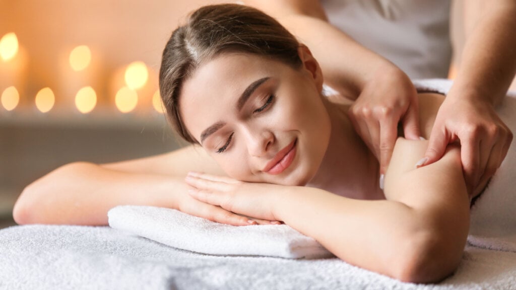 Mulher sorrindo deitada recebendo massagem nos braços