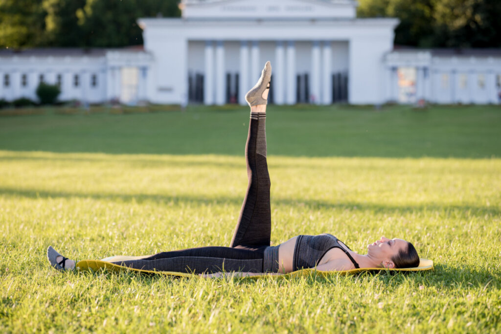 Mulher deitada na grama fazendo o exercício one leg circle.