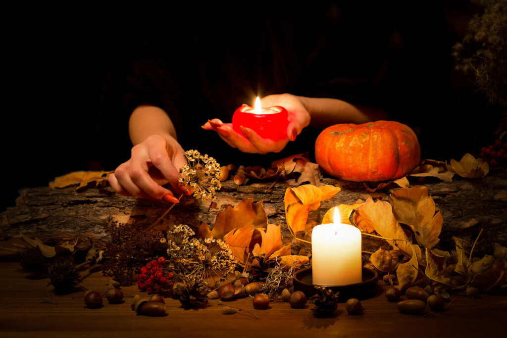 Mãos femininas mexendo em plantas em uma mesa com velas e abóbora