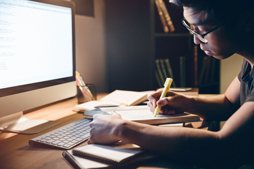 Jovem estudando com livros e o computador ligado