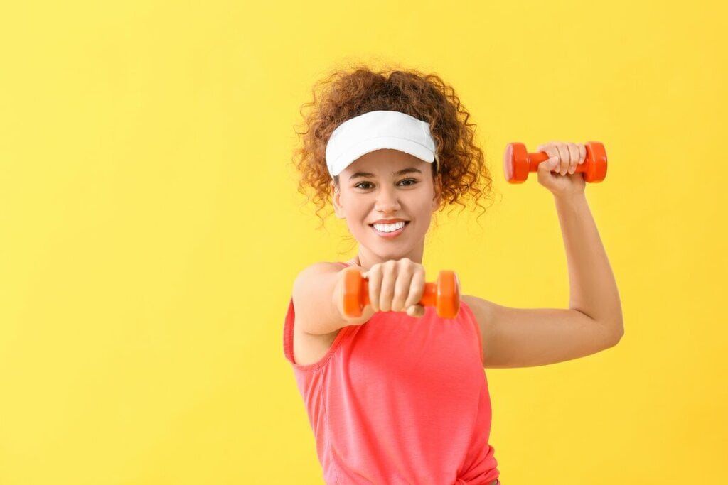 Menina usando boné branco e blusa rosa segurando um peso de academia rosa