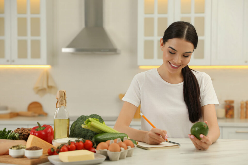 Mulher em uma cozinha rodeada de alimentos e escrevendo em um papel