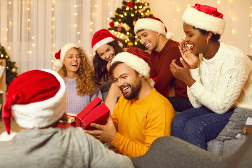 Pessoas com gorro de natal reunidas ao redor de uma árvore de Natal trocando presentes