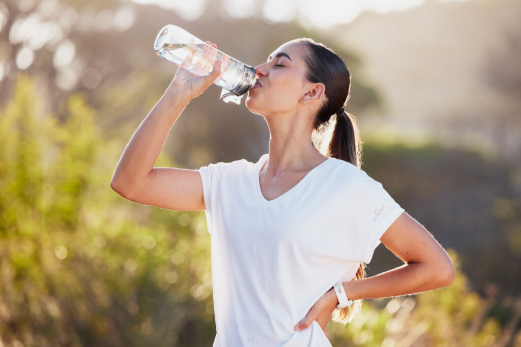 Mulher bebendo água após corrida esportiva na natureza