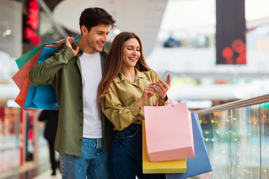 Homem e mulher com sacolas de compras e olhando para o celular