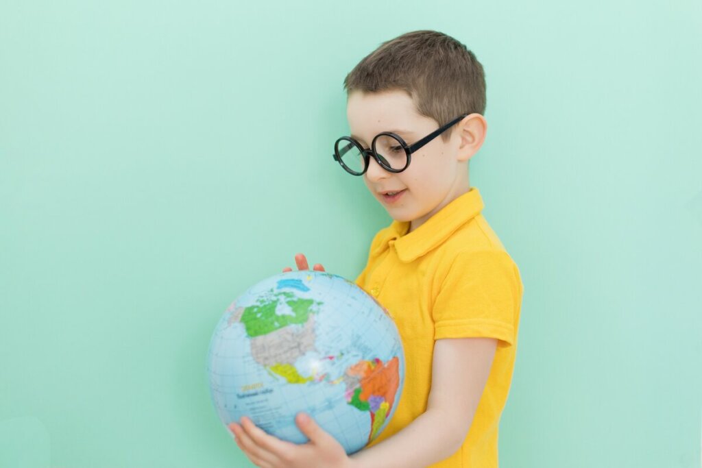 Menino usando óculos e blusa amarela segurando um globo terrestre