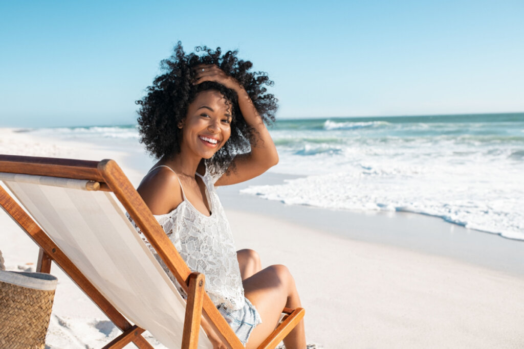 Mulher tomando banho de sol em uma espreguiçadeira na praia enquanto olha para a câmera