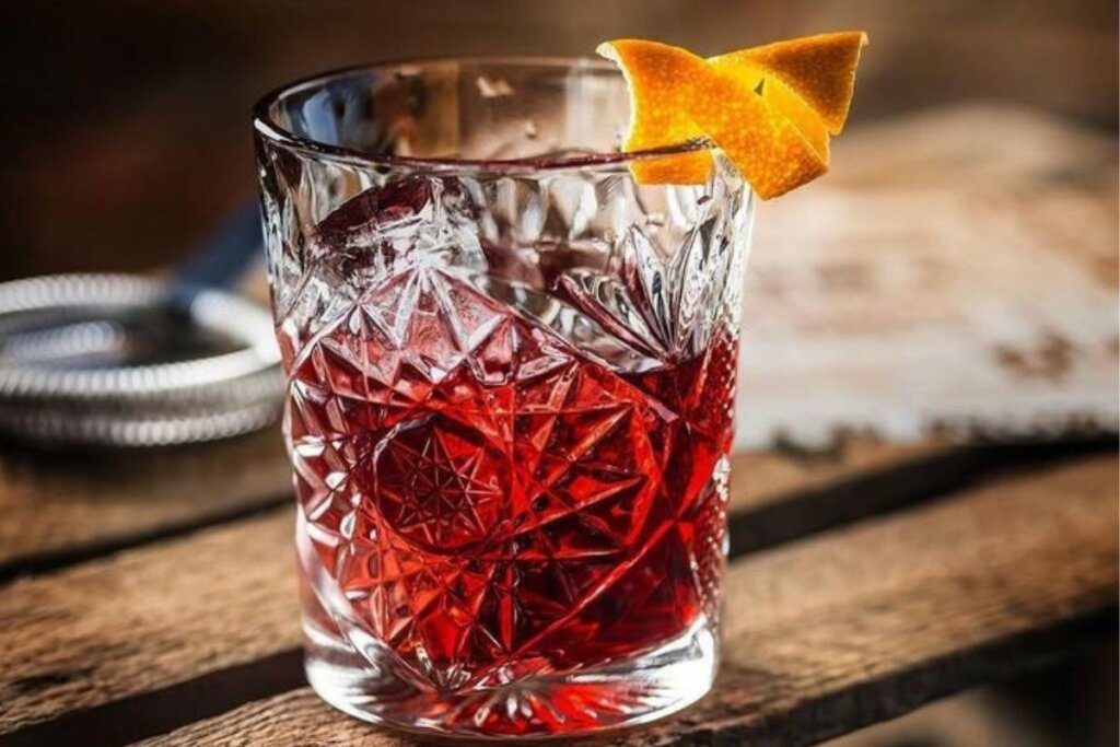 Copo de vidro com drink vermelho decorado com casca de laranja