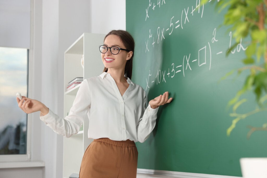 Professora jovem explicando equações matemáticas de potenciação no quadro-negro em sala de aula