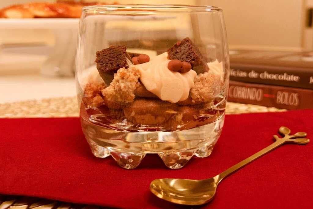 Copo de vidro com verrine três chocolates em cima de pano vermelho e colher ao lado