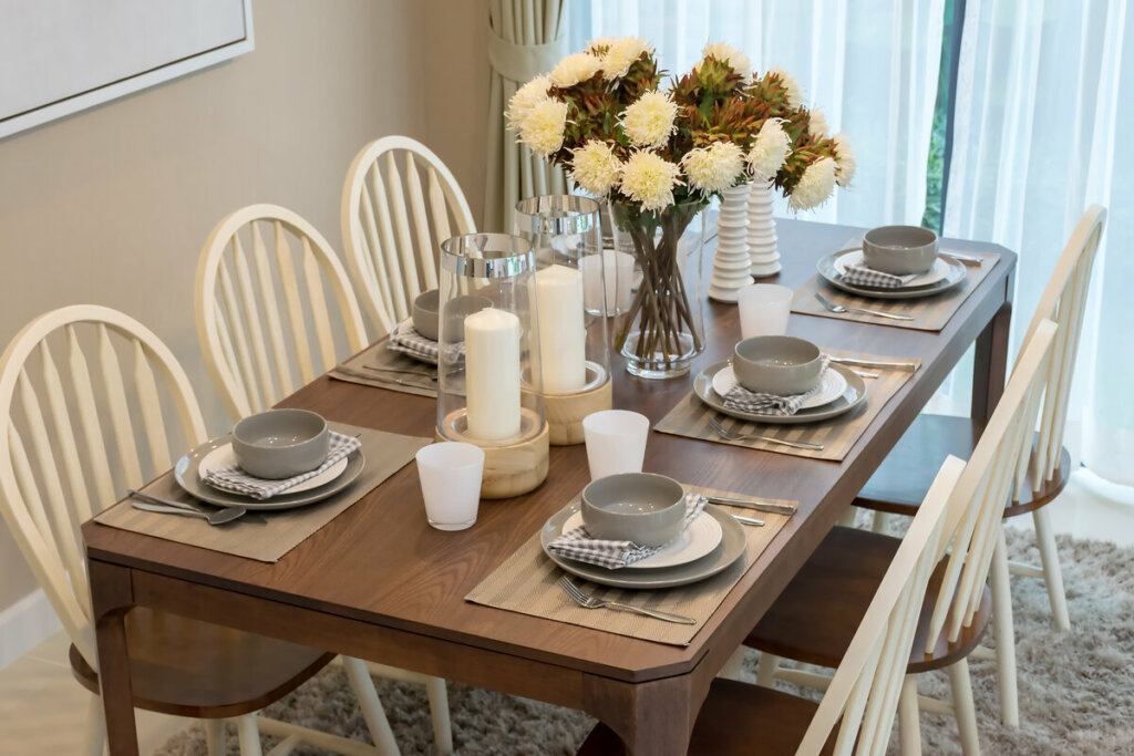 Mesa de jantar de madeira com pratos brancos e cinza, arranjo de flores brancas e velas brancas 