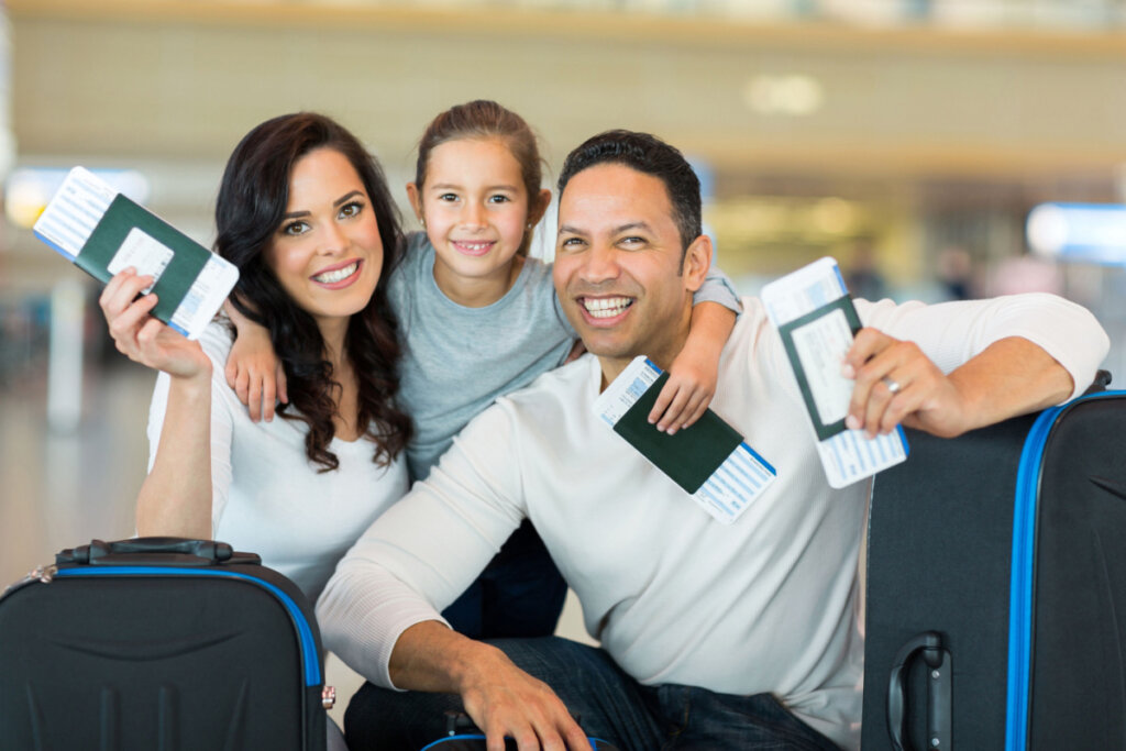 Família sorrindo com malas e documentos para viajar em mãos