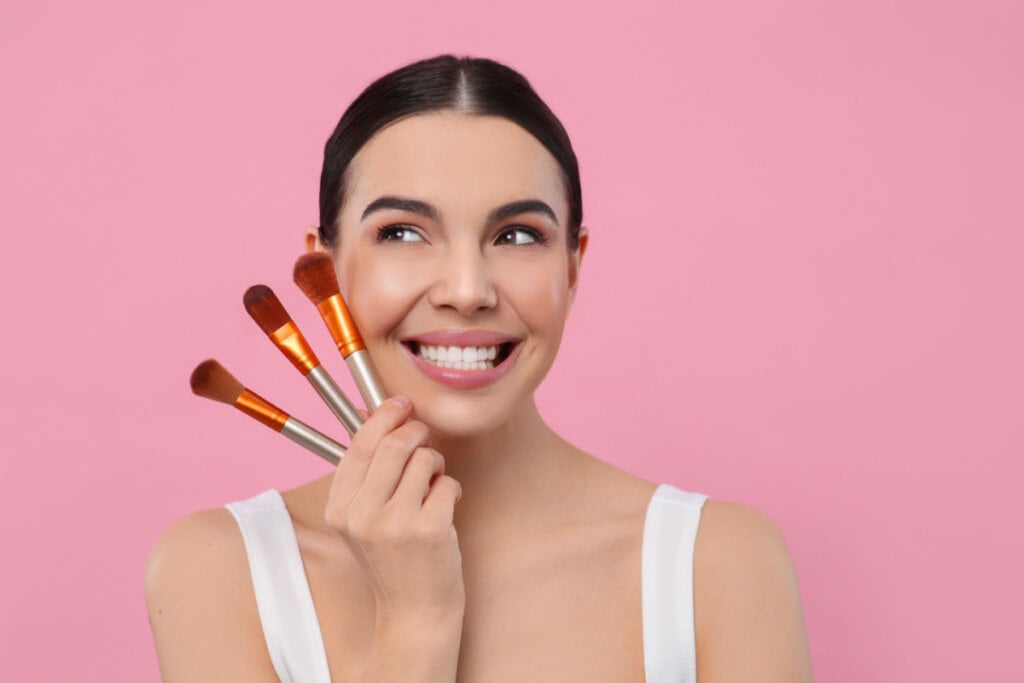 Mulher sorrindo e segurando 3 pincéis de maquiagem