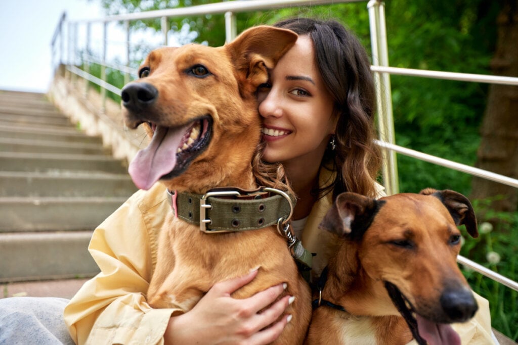 Mulher abraçada em dois cachorros marrons