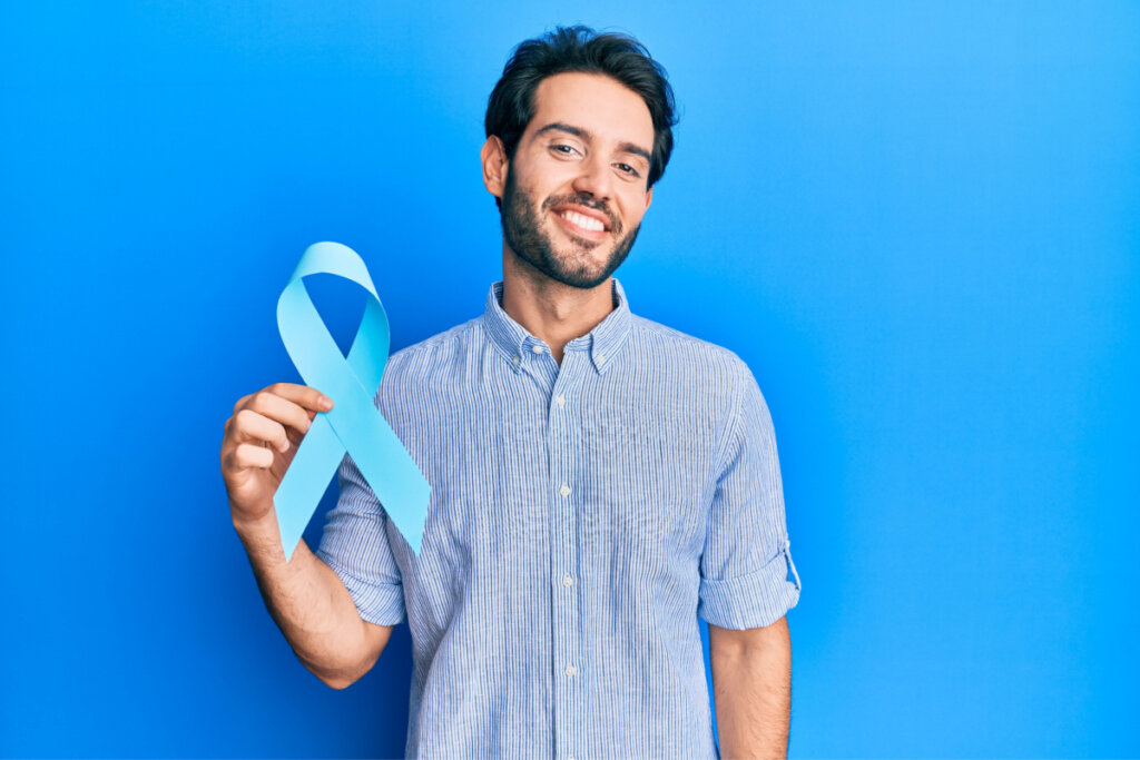 Homem de camisa azul segurando laço azul. Ele está em fundo azul