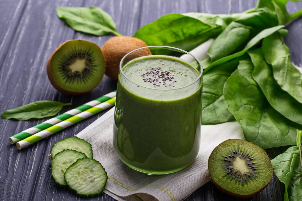 Copo de vidro com suco verde e semente de chia. Espinafre, kiwi e pepino em volta do copo