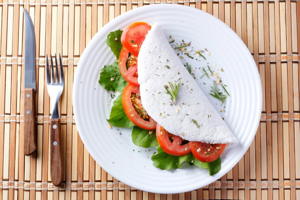 Tapioca com tomate e rúcula em cima de um prato branco