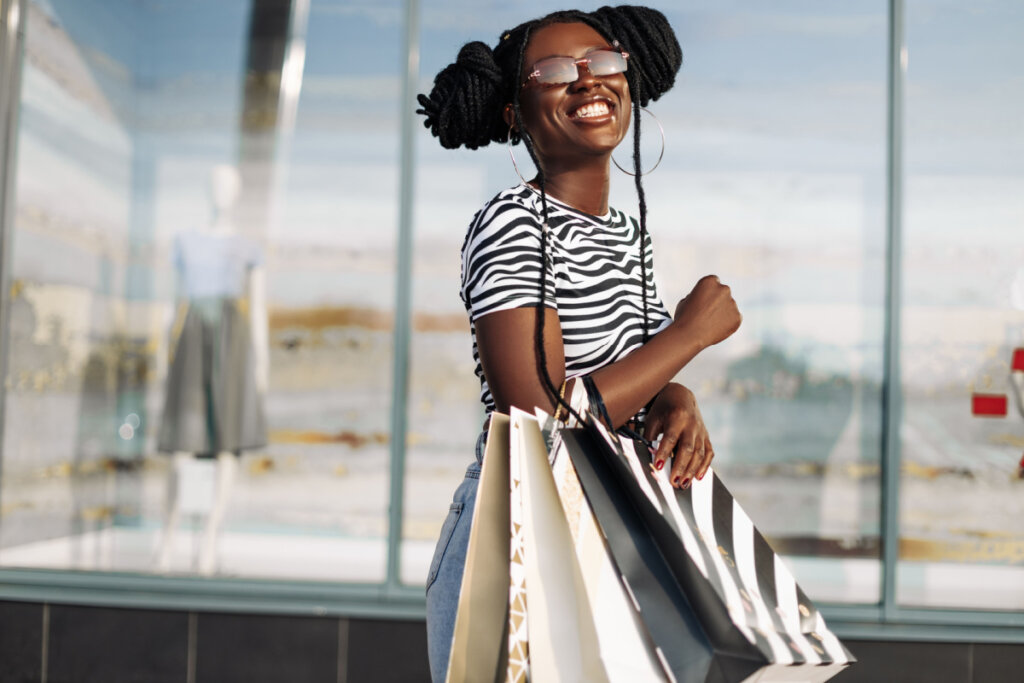 Mulher negra sorrindo com sacolas no braço