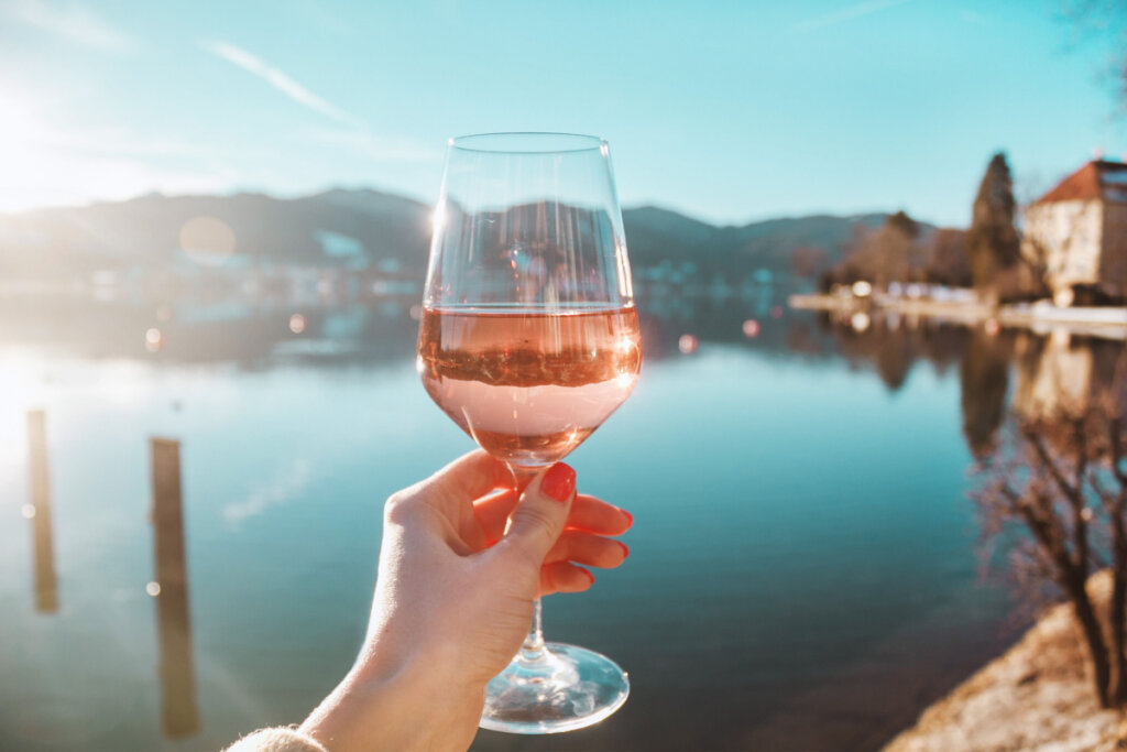 Mão feminina segurando taça de vinho rosé na na costa do lago Tegernsee