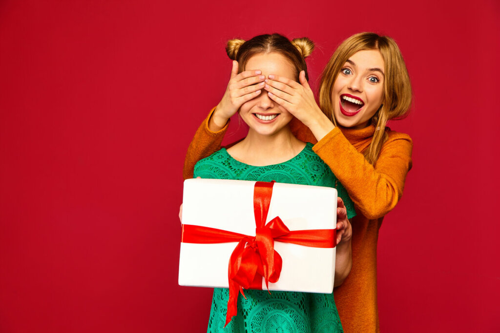 Mulher tapando os olhos de uma menina segurando uma caixa de presente