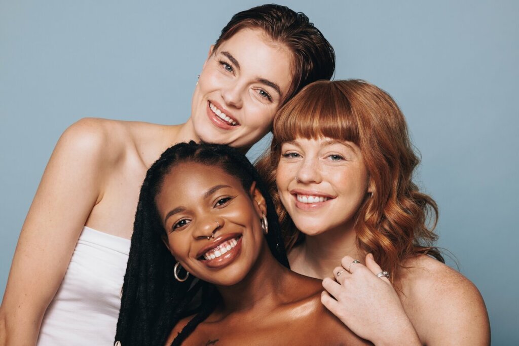 Três mulheres juntas em frente a um fundo azul sorrindo