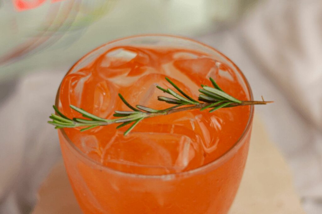 Copo de vidro com drink laranja e pedras de gelo