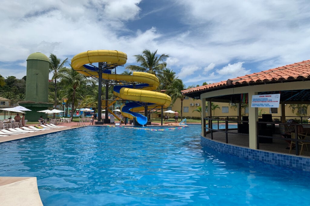 Piscina com água azul e tobogã amarelo ao fundo