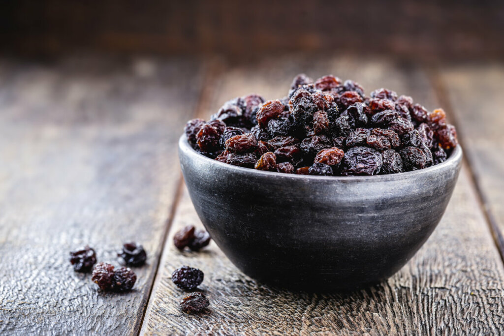 Uvas-passas em um recipiente preto em cima de uma mesa de madeira