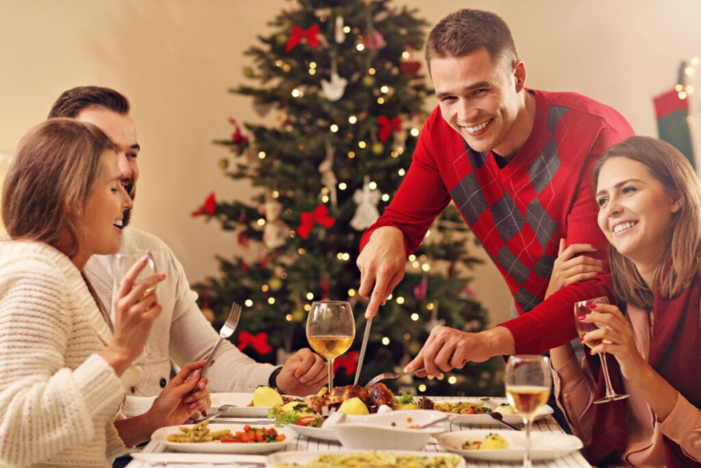 Homem cortando comida na mesa de natal com outras três pessoas