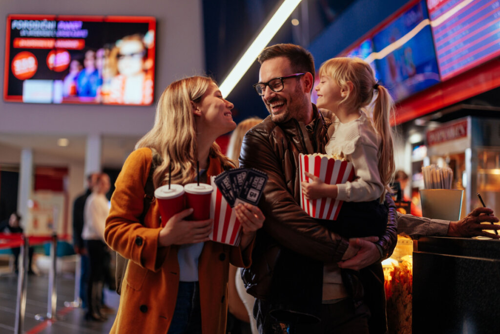 Mulher, homem e menina segurando pipoca, refrigerante e entradas para o cinema