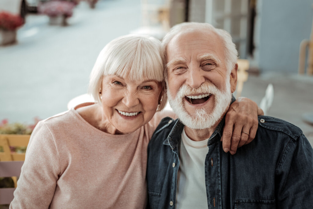 Mulher e homem idosos sorrindo e se abraçando de lado