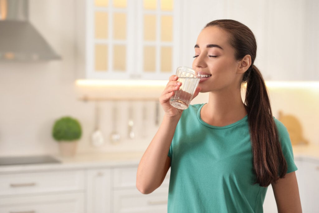 Mulher bebendo um copo de água na cozinha 