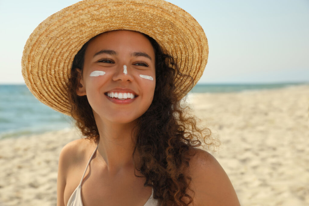 Mulher sorrindo na praia com protetor solar no rosto