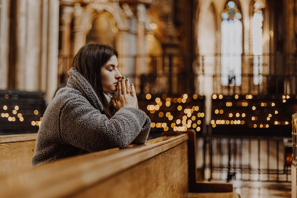 Mulher rezando ajoelhada em igreja