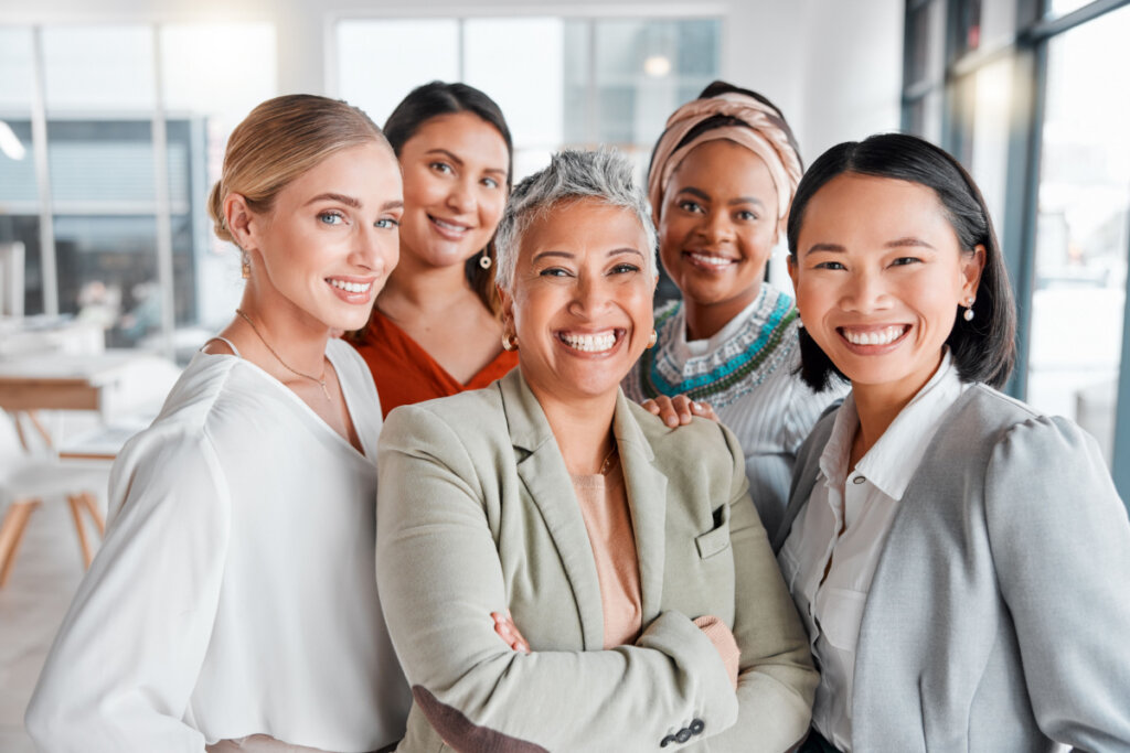 Cinco mulheres uma ao lado da outra com roupa de trabalho e sorrindo