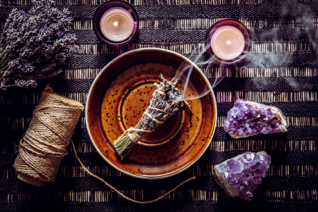 Maço de lavanda sendo queimado, com cristais de amestistas e velas ao lado