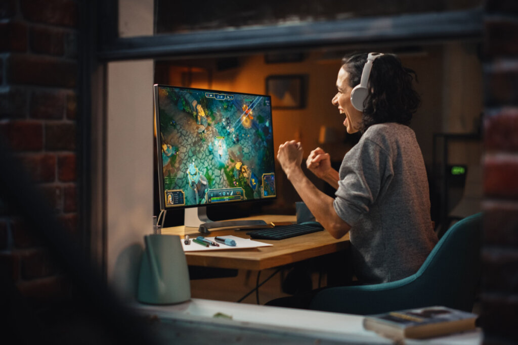 Mulher sentada em frente a computado comemorando jogo de videogame