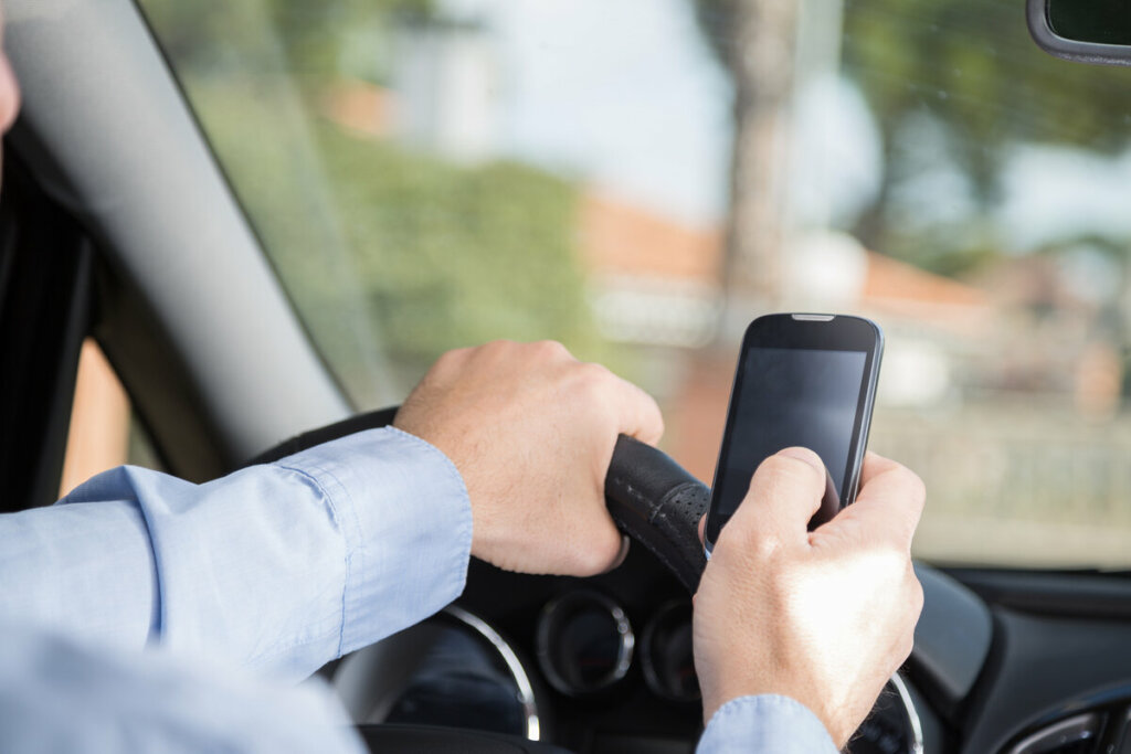 Mãos masculinas no volante de um carro segurando um celular 